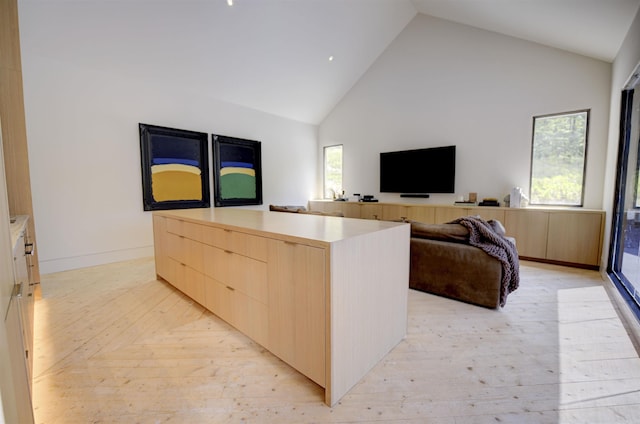 interior space featuring modern cabinets, a kitchen island, light countertops, light brown cabinets, and high vaulted ceiling