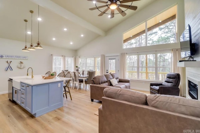 living area featuring a wealth of natural light, light wood-style flooring, beam ceiling, and a glass covered fireplace