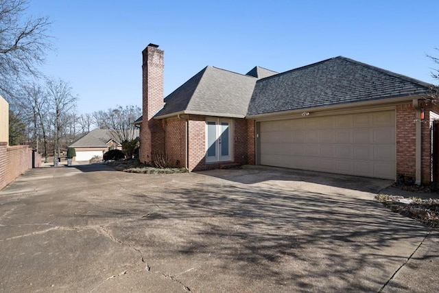 view of side of home featuring roof with shingles, brick siding, a chimney, fence, and driveway