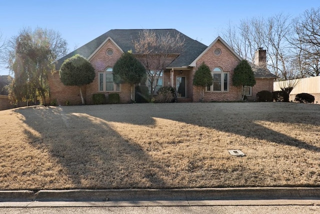 ranch-style home with brick siding, a chimney, a front lawn, and fence