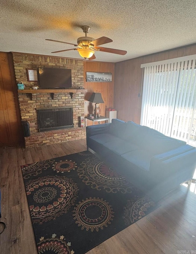 living room featuring a textured ceiling, wooden walls, a fireplace, and wood finished floors