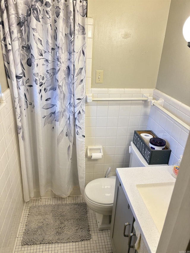 bathroom featuring toilet, a wainscoted wall, tile patterned flooring, and tile walls