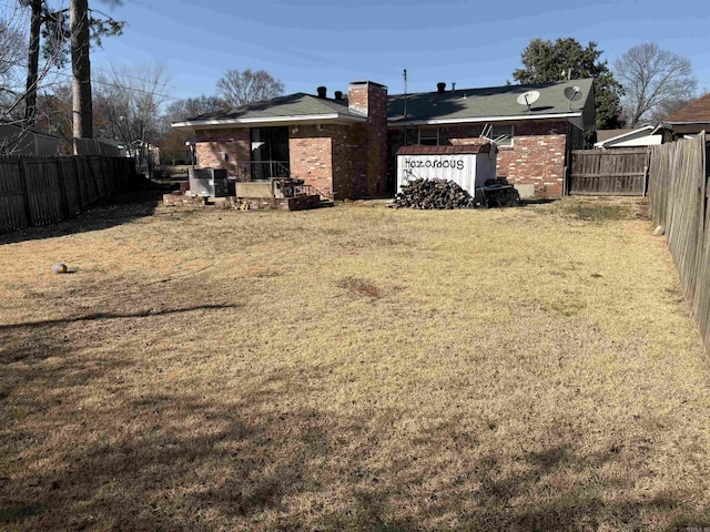 rear view of house with brick siding, a lawn, a chimney, and a fenced backyard