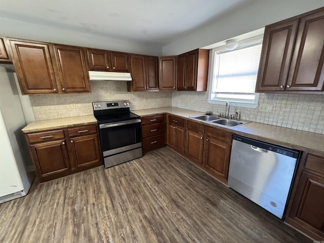 kitchen with dark wood finished floors, stainless steel appliances, backsplash, a sink, and under cabinet range hood