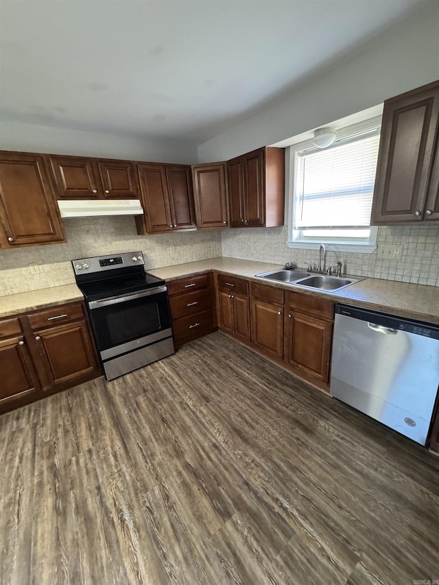 kitchen with dark wood finished floors, appliances with stainless steel finishes, light countertops, under cabinet range hood, and a sink