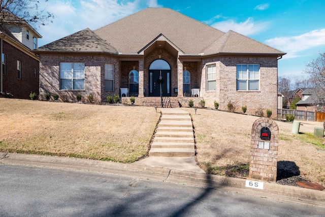 view of front of property with brick siding, roof with shingles, and a front yard