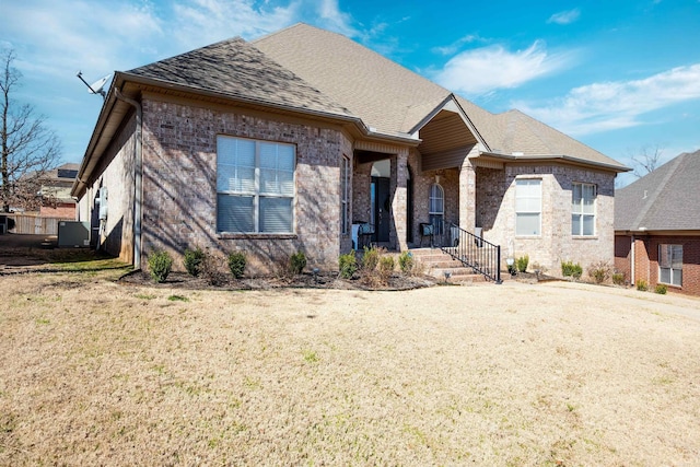 view of front of home featuring roof with shingles, brick siding, and a front lawn