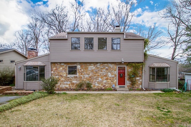 colonial inspired home featuring a front yard, stone siding, a chimney, and entry steps