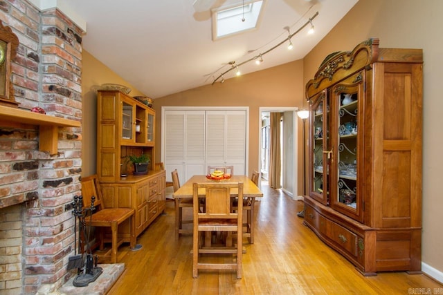 dining room with baseboards, vaulted ceiling, light wood-style floors, a brick fireplace, and rail lighting