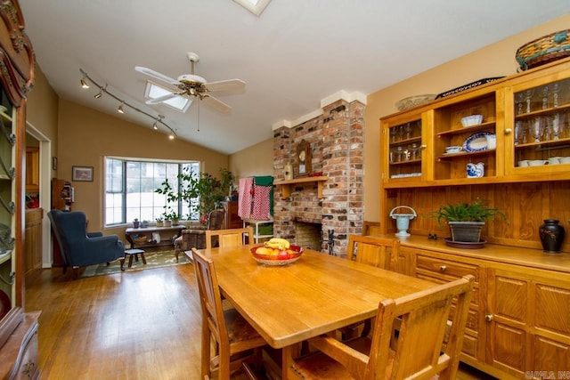 dining space featuring ceiling fan, a brick fireplace, vaulted ceiling, and wood finished floors