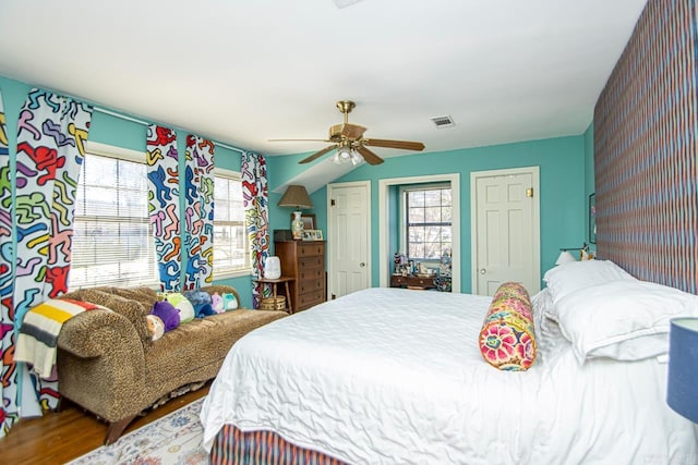 bedroom with multiple closets, a ceiling fan, visible vents, and wood finished floors