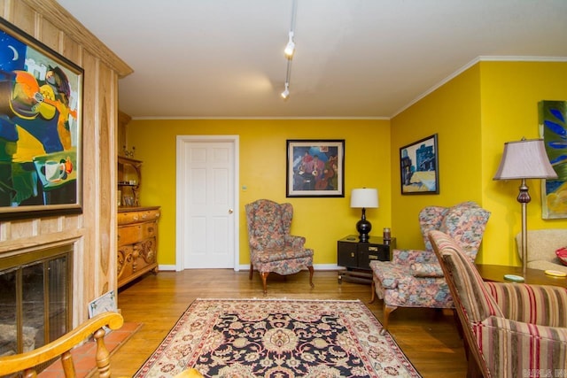 sitting room featuring a glass covered fireplace, crown molding, baseboards, and wood finished floors