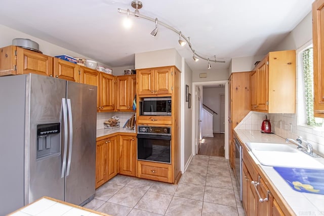 kitchen with tile countertops, light tile patterned floors, backsplash, appliances with stainless steel finishes, and a sink