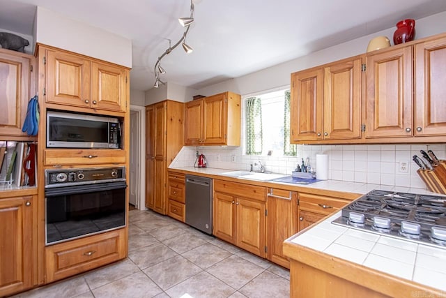 kitchen with tile countertops, light tile patterned flooring, a sink, appliances with stainless steel finishes, and tasteful backsplash