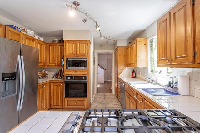 kitchen with decorative backsplash, tile countertops, appliances with stainless steel finishes, a sink, and light tile patterned flooring