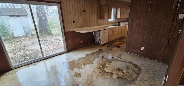 kitchen with light countertops, white dishwasher, wood walls, and a sink