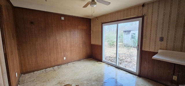 unfurnished room featuring wood walls, plenty of natural light, wallpapered walls, and a ceiling fan