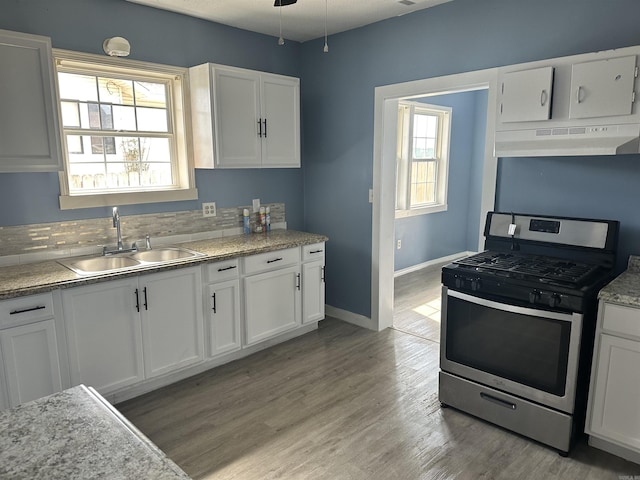 kitchen with stainless steel gas stove, light wood finished floors, under cabinet range hood, white cabinetry, and a sink