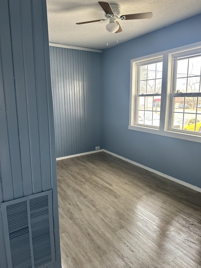 empty room featuring a ceiling fan, a textured ceiling, visible vents, and wood finished floors