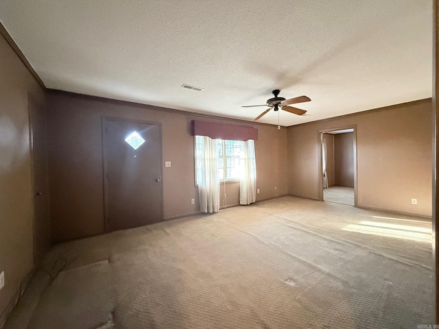 foyer entrance featuring a textured ceiling, light colored carpet, a ceiling fan, visible vents, and ornamental molding