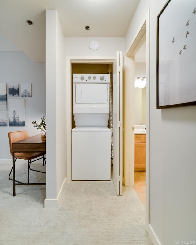 laundry room featuring stacked washing maching and dryer, baseboards, laundry area, and light colored carpet