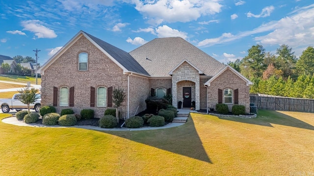 french country home with a front yard, brick siding, fence, and roof with shingles