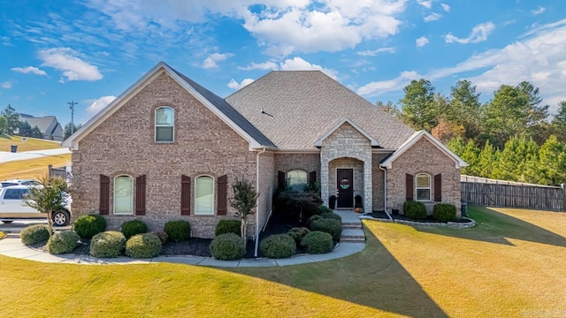 view of front of property featuring a front lawn, a shingled roof, fence, and brick siding