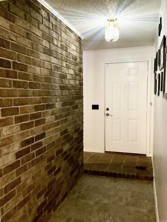 doorway to outside featuring a textured ceiling, brick wall, and dark tile patterned floors