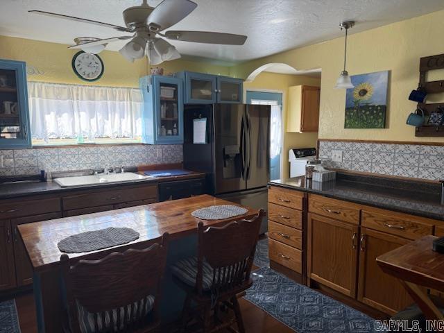 kitchen with refrigerator with ice dispenser, decorative backsplash, a sink, decorative light fixtures, and glass insert cabinets