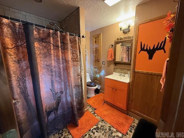 bathroom with curtained shower, a wainscoted wall, toilet, vanity, and a textured ceiling