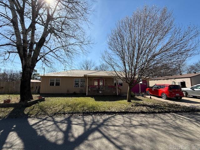 single story home with metal roof, covered porch, a front yard, and fence