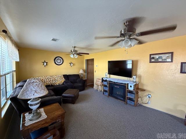 living area with visible vents, ceiling fan, carpet, and a textured wall