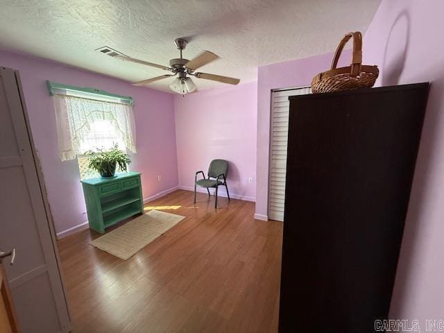 unfurnished room featuring visible vents, baseboards, ceiling fan, wood finished floors, and a textured ceiling