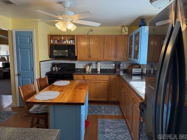 kitchen featuring black appliances, a kitchen breakfast bar, backsplash, butcher block counters, and glass insert cabinets