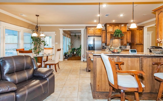 kitchen with light tile patterned floors, light stone counters, open floor plan, stainless steel fridge with ice dispenser, and brown cabinetry