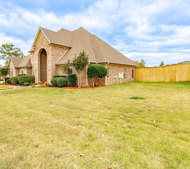 view of side of home with a yard, brick siding, a shingled roof, and fence