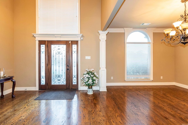 foyer entrance featuring visible vents, a notable chandelier, ornate columns, and wood finished floors