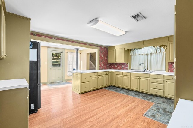 kitchen featuring visible vents, freestanding refrigerator, a sink, a peninsula, and wallpapered walls