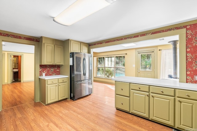 kitchen with light wood finished floors, freestanding refrigerator, a peninsula, light countertops, and green cabinets