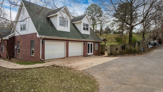 view of front of home featuring driveway, a shingled roof, french doors, and brick siding