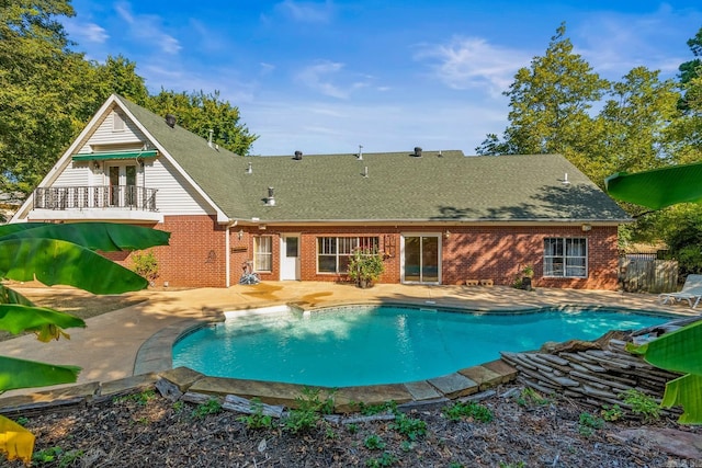 back of property featuring roof with shingles, an outdoor pool, a patio, and brick siding