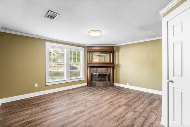 unfurnished living room with a tile fireplace, wood finished floors, visible vents, baseboards, and ornamental molding