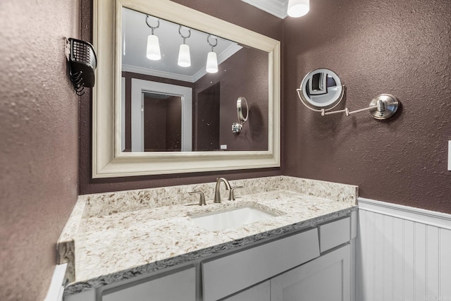 bathroom with a textured wall, ornamental molding, wainscoting, and vanity