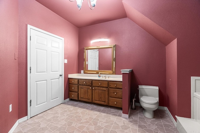 bathroom with toilet, stone finish floor, vaulted ceiling, vanity, and baseboards