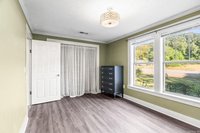 unfurnished bedroom with a textured ceiling, wood finished floors, visible vents, baseboards, and crown molding