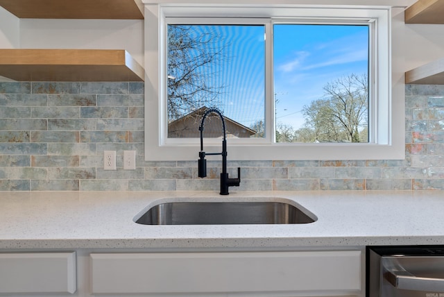 kitchen featuring tasteful backsplash, white cabinets, dishwasher, light stone countertops, and a sink