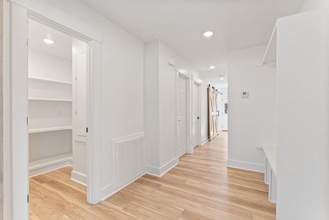 corridor featuring light wood finished floors, a barn door, visible vents, and recessed lighting