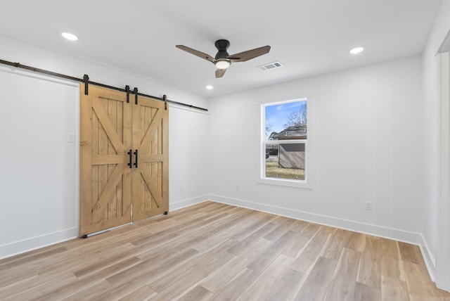 empty room featuring light wood finished floors, a barn door, visible vents, and baseboards