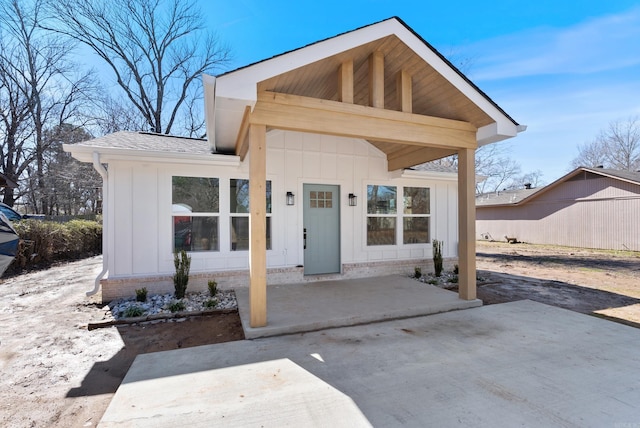 view of exterior entry featuring roof with shingles, board and batten siding, and a patio area