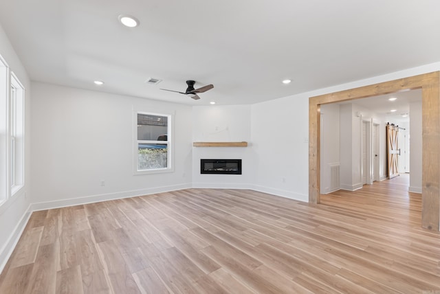 unfurnished living room featuring light wood finished floors, visible vents, baseboards, a glass covered fireplace, and recessed lighting